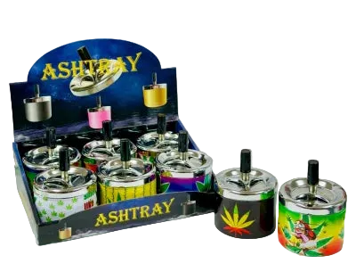 A retail display box and three individual printed spinning ashtrays shown on a stylized teal and gray background. The ashtrays feature colorful graphics including a cannabis leaf and tropical illustrations, with metallic silver bases and black tops.